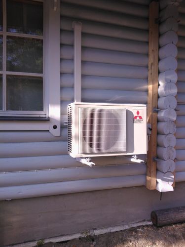 Ilmalämpöpumpun ulkoyksikkö siististi asennettuna hirsimökin seinässä.