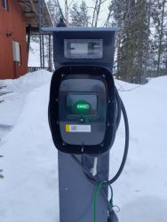 Sähköauton lataustolppa lumisessa maisemassa.
