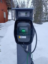 Sähköauton lataustolppa lumisessa maisemassa.